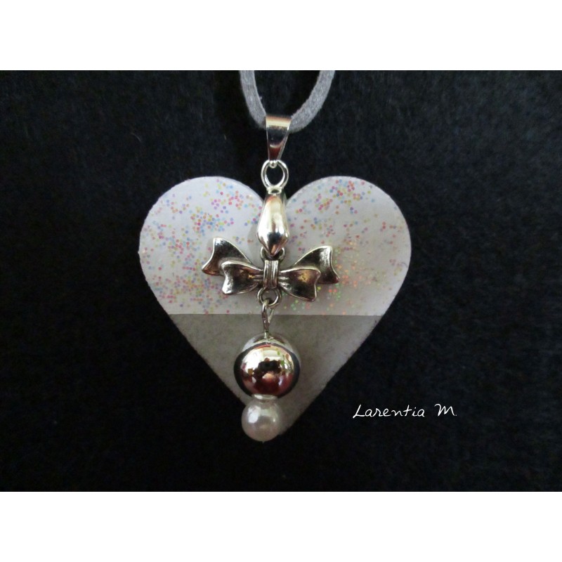 Collier pendentif avec perles cirées argent/blanche, suspendues à un noeud papillon, sur socle de béton coeur blanc pailleté